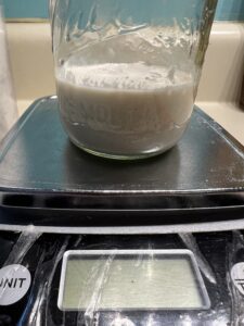 100% hydration starter in a mason jar on top of a well loved kitchen scale, display turned off.